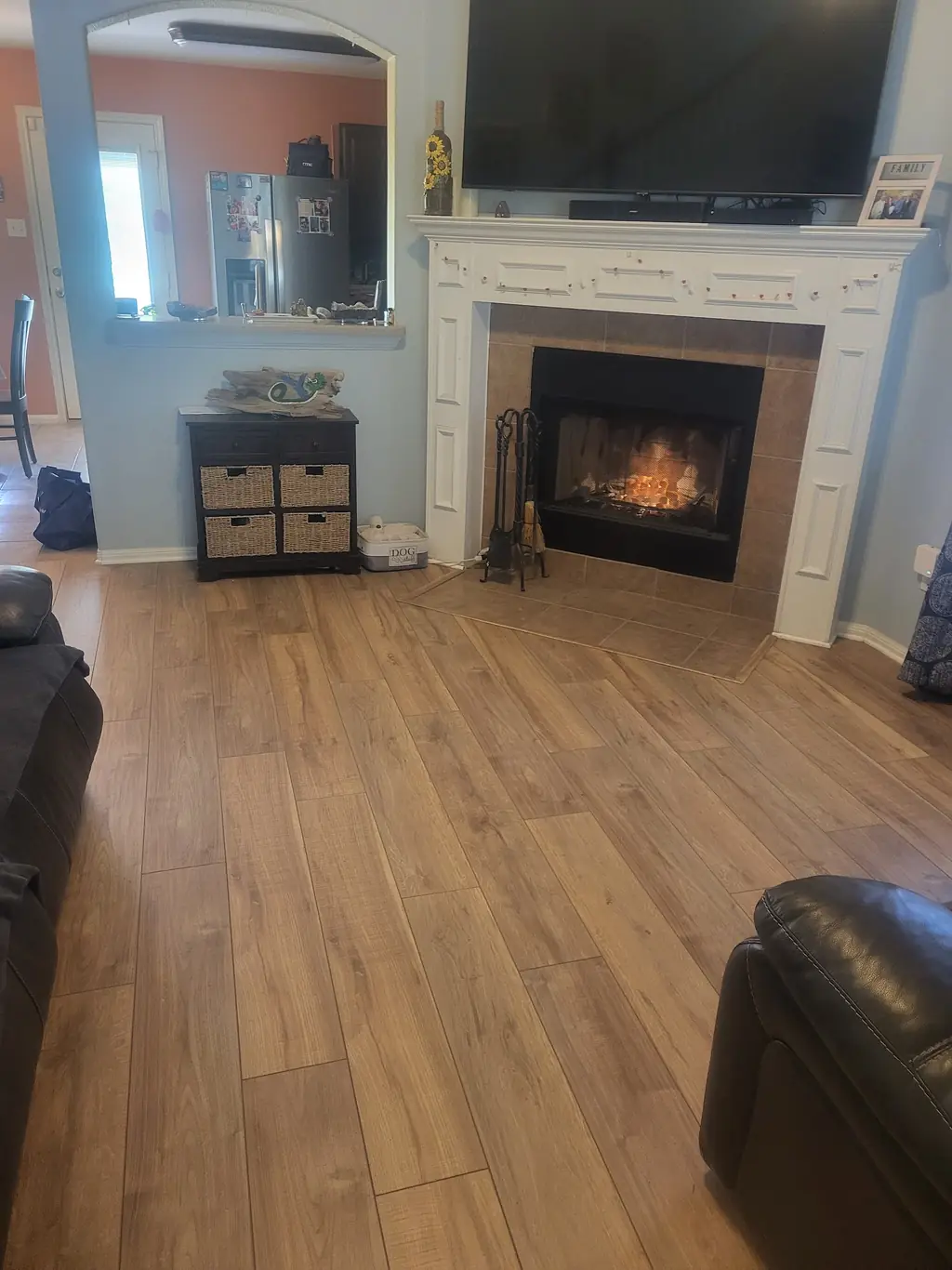 Living room in new laminate flooring meeting the tiled hearth of a lit fireplace